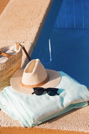 A beach towel, a straw hat, sunglasses, and a woven bag by a pool.