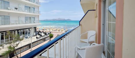 Un balcon avec vue sur la plage et l’océan, des meubles en osier blancs et un immeuble à plusieurs étages doté de balcons.