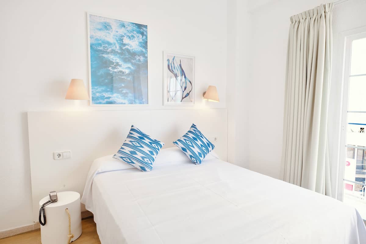 A hotel room with a bed, two wall-mounted lamps, a telephone, and two artworks.