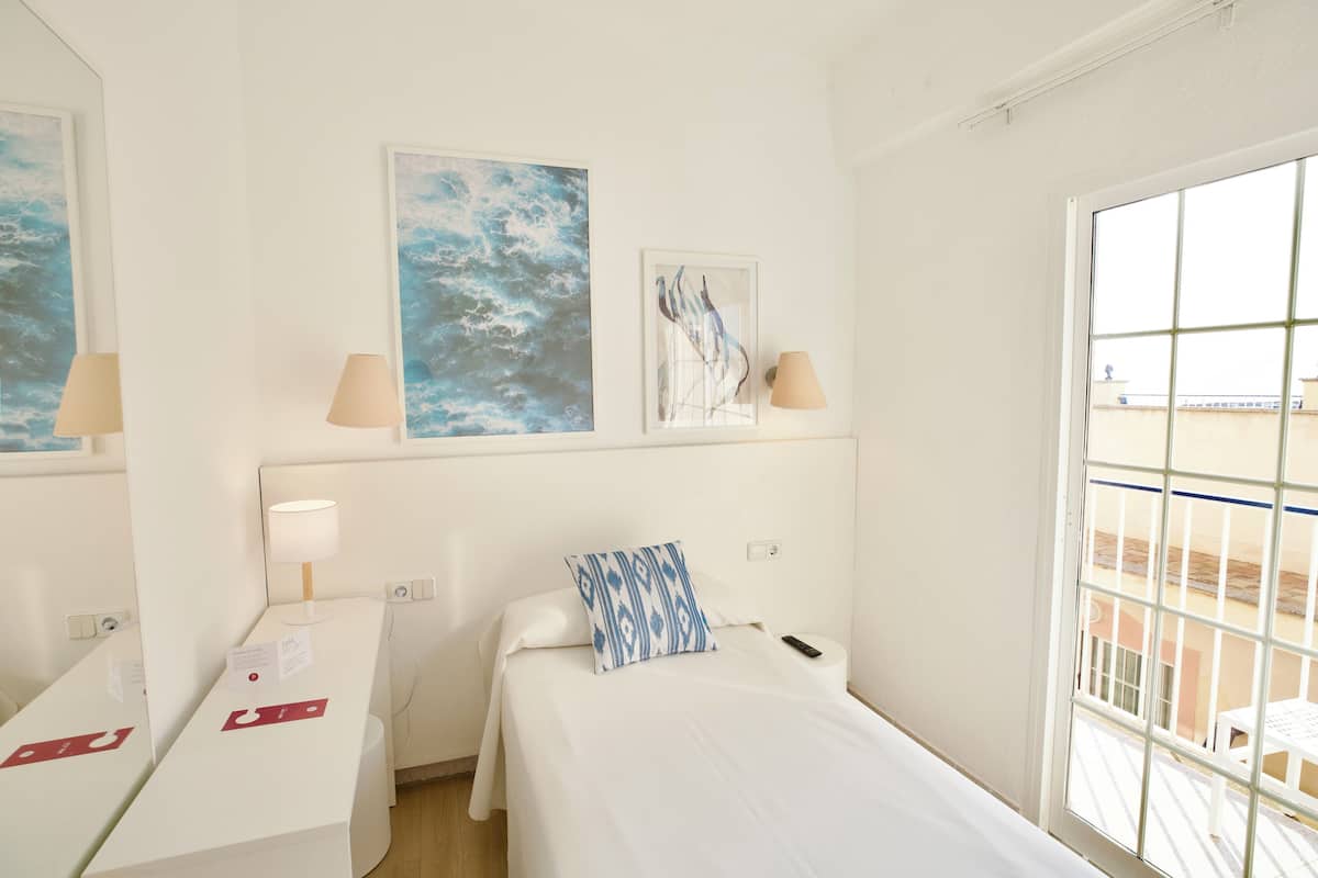 A hotel room with a bed, a desk, two lamps, and artwork on the walls.