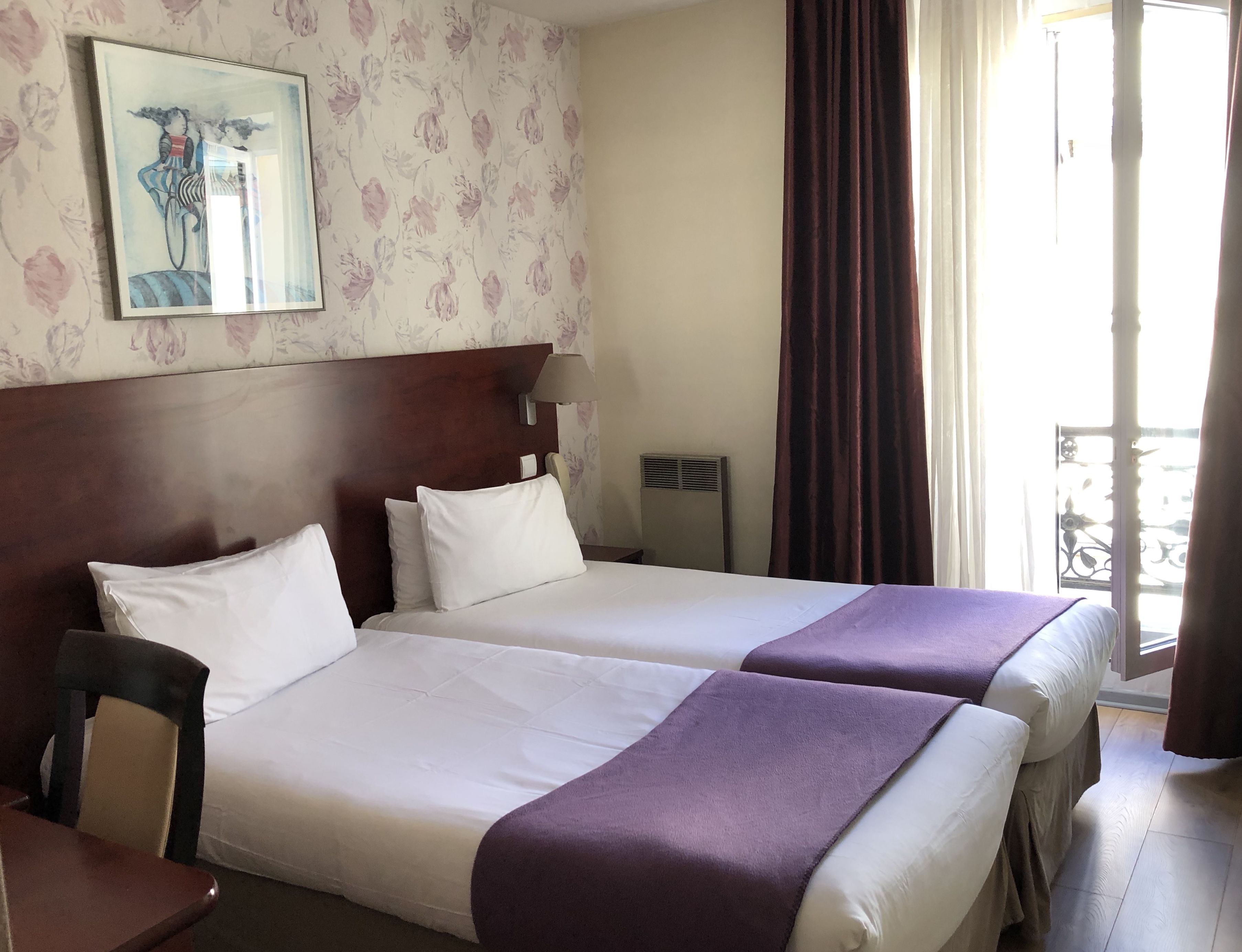 A hotel room with two beds, a wooden headboard, a painting on the wall, a window with curtains, and a chair.