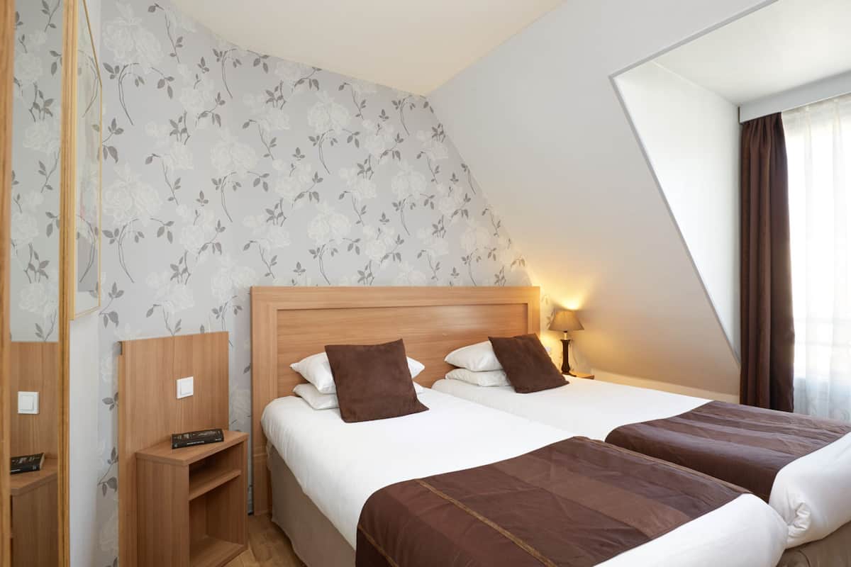 A hotel room with two beds, a wooden headboard, a nightstand, and a mirror.
