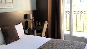 A hotel room with a large bed, a desk with a lamp, a television, and a balcony with curtains. - Hotel Alane (Paris)