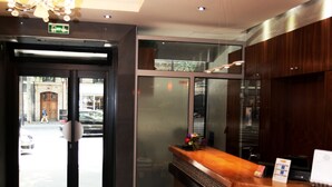 A reception area with a wooden counter, a chandelier, and a glass door leading outside. - Hotel Alane (Paris)