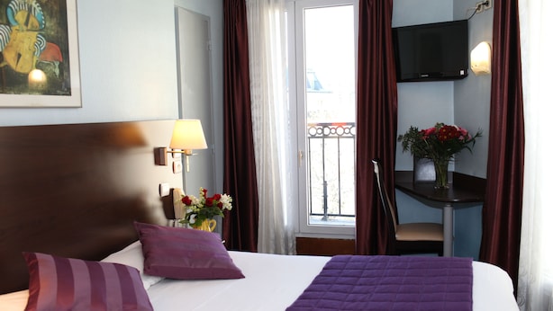 A hotel room with a large bed, a desk with a chair, a TV mounted on the wall, and a balcony with curtains. - Hotel Alane (Paris)