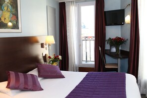 A hotel room with a large bed, a desk with a chair, a TV mounted on the wall, and a balcony with curtains. - Hotel Alane (Paris)