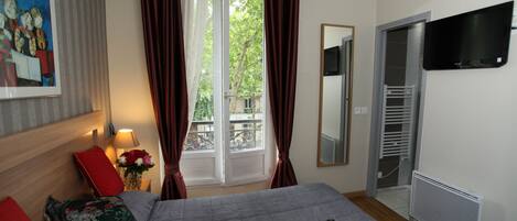 Una habitación de hotel con cama, televisión, calefacción y ventana con cortinas.