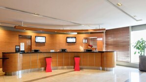 A modern reception desk with a curved design, two red stools, and a large window with blinds. - ibis Ambassador Seoul Myeongdong (Seoul)
