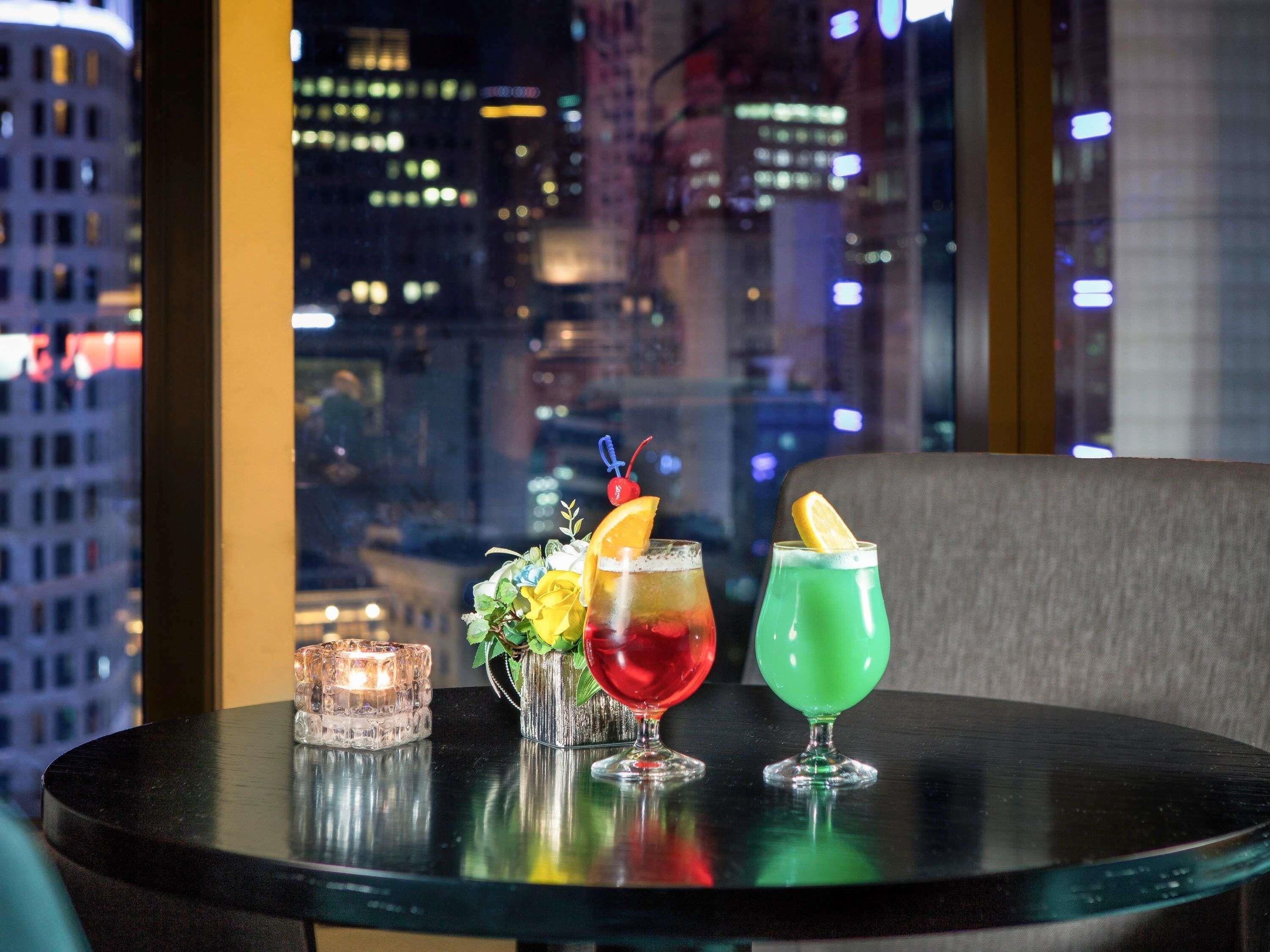 A table with three cocktails, a candle, and a vase with flowers.