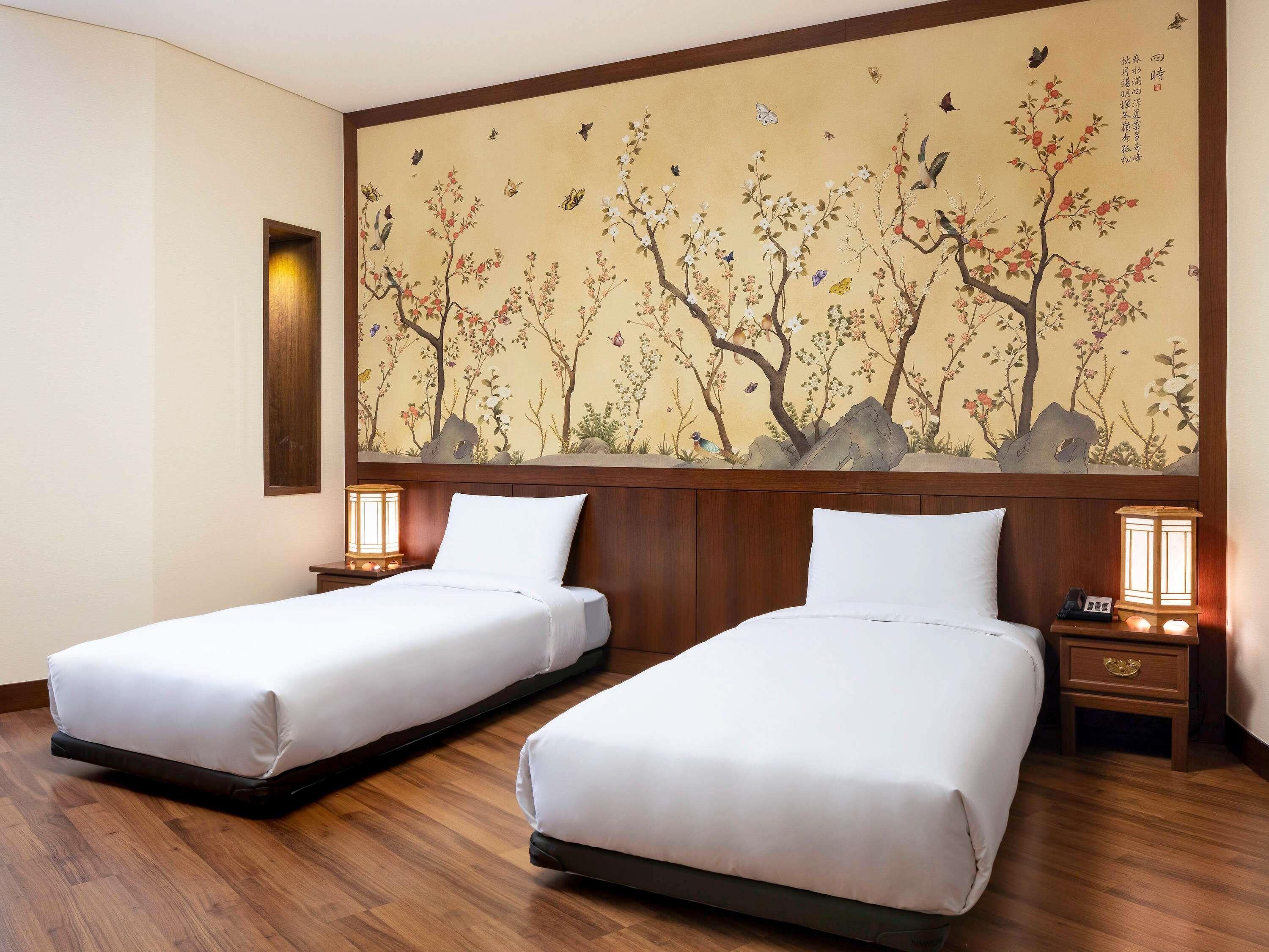 A hotel room with two beds, wooden headboards, a large wall mural, and bedside lamps.