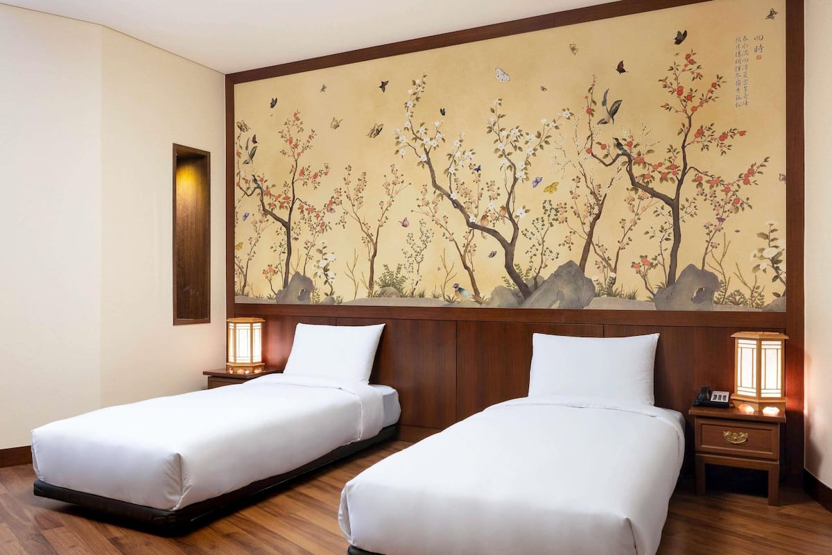 Ein Hotelzimmer mit zwei Betten, Holz-Kopfteilen, einem großen Wandbild und Nachttischlampen.