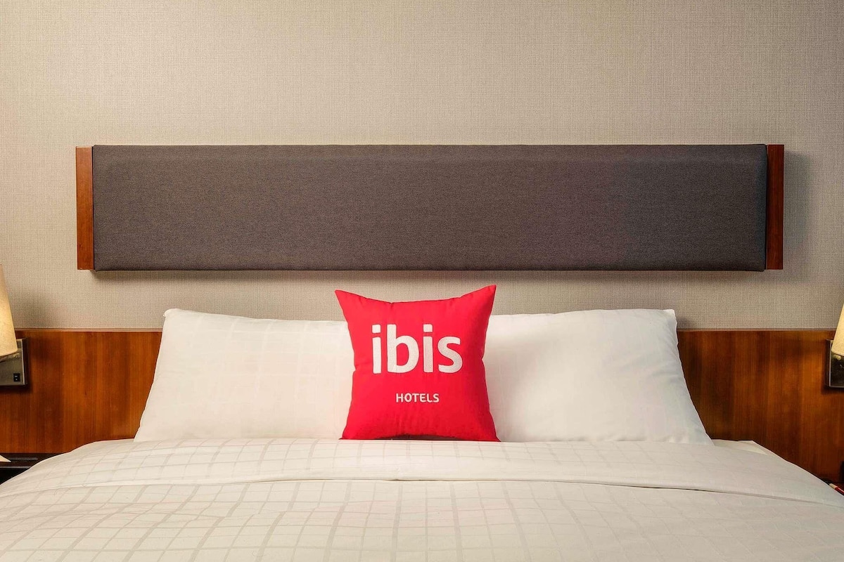 A hotel room with a bed, a headboard, and two bedside lamps.