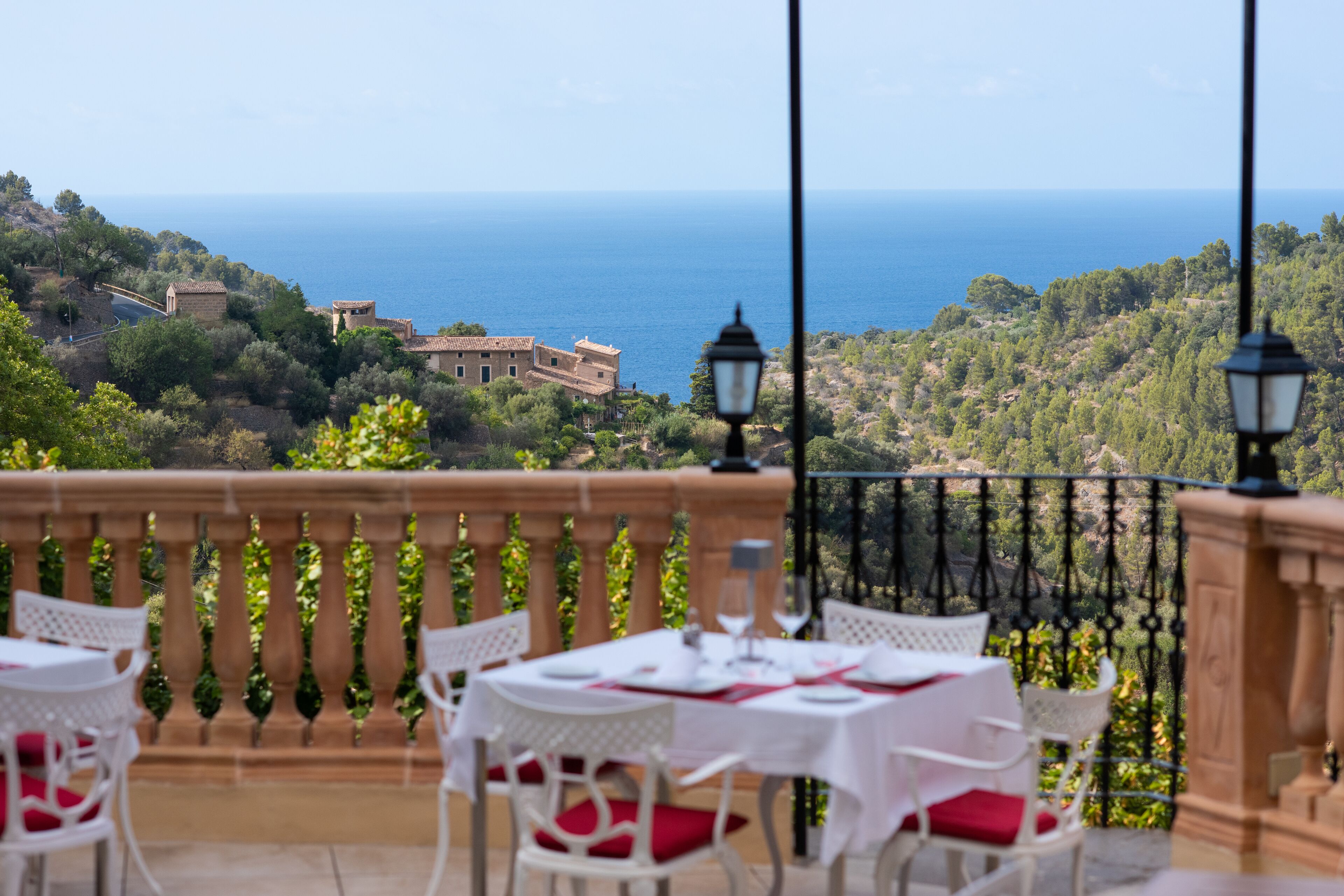 A terrace with white tables and chairs, a view of the sea, and a stone balustrade.