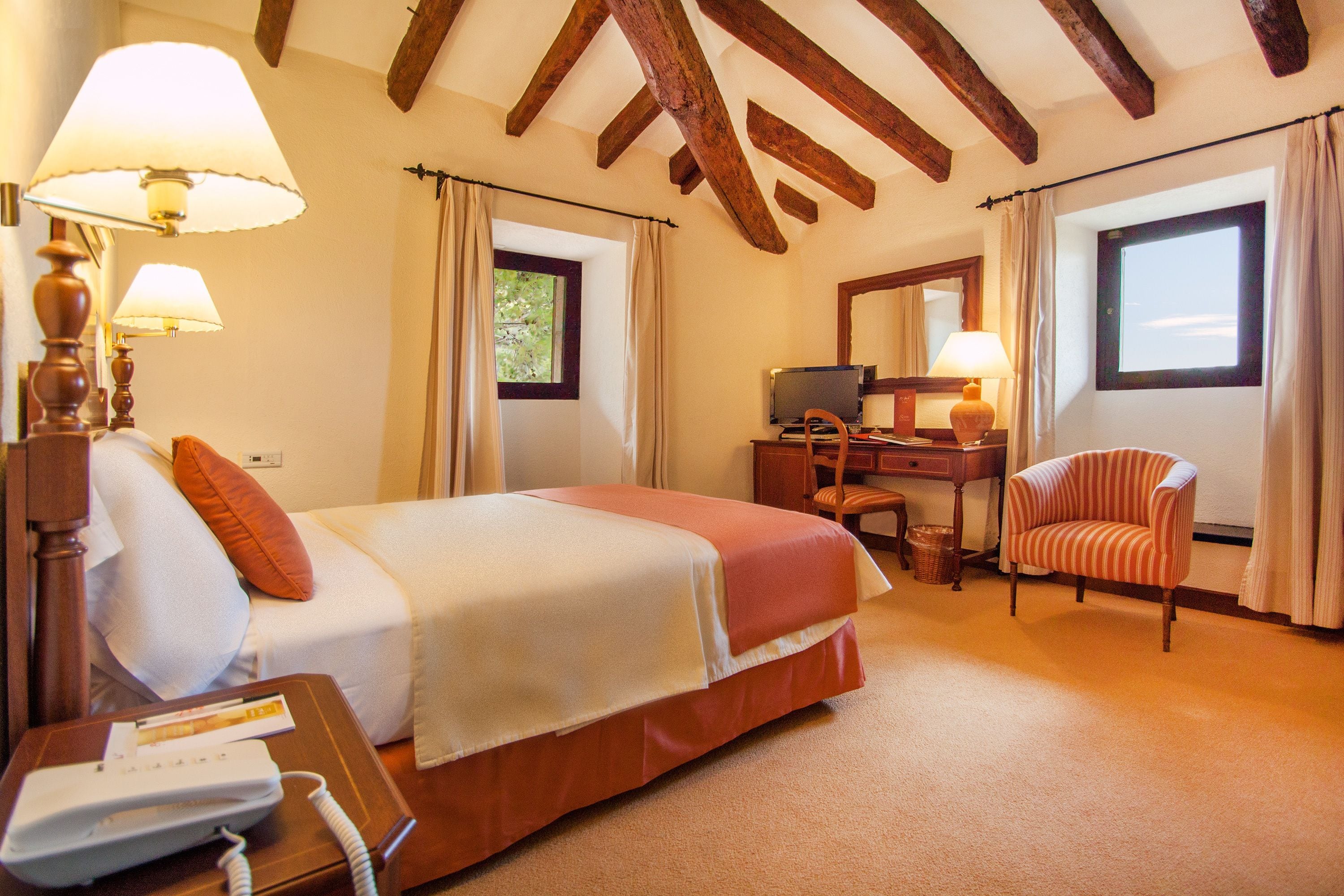 Una habitación de hotel con cama, escritorio con lámpara, silla y televisión.