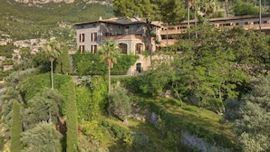 A stone building with multiple balconies, surrounded by lush greenery and mountains in the background. - Es Moli Hotel (Deià)