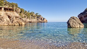 A coastal scene with clear water, rocky cliffs, and a wooden structure on the left. - Es Moli Hotel (Deià)