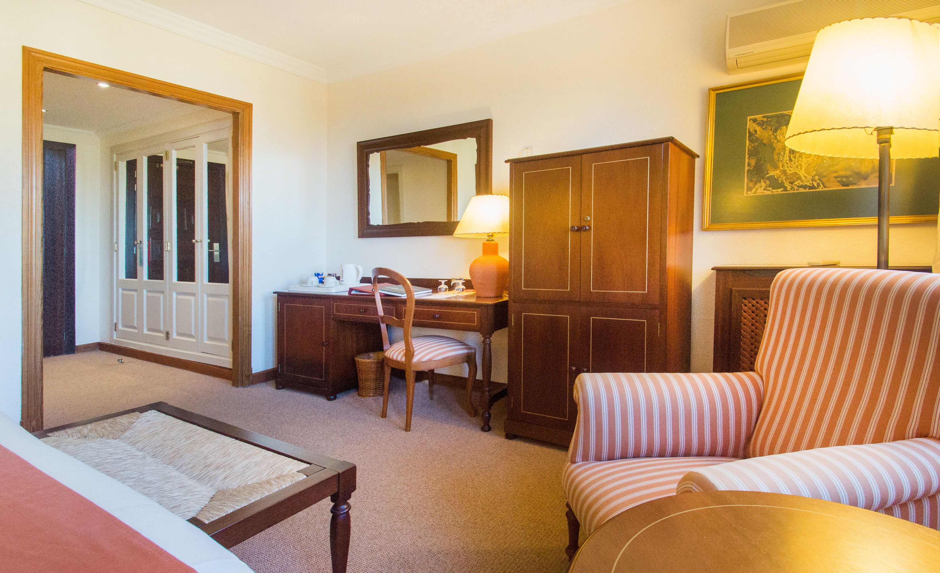 Habitación de hotel con cama, escritorio, silla, armario, espejo y lámpara.