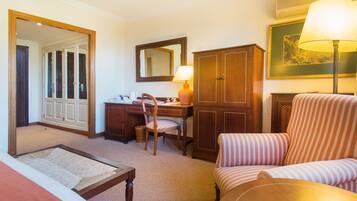 Habitación de hotel con cama, escritorio, silla, armario, espejo y lámpara.