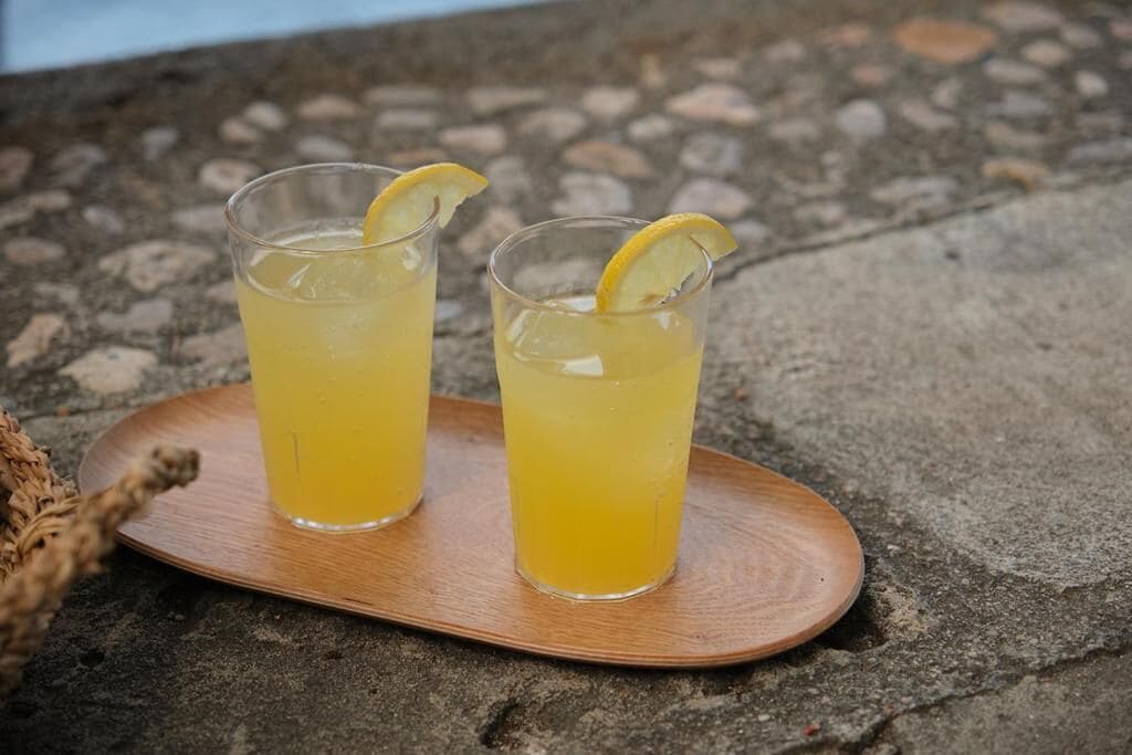Two glasses of yellow beverage on a wooden tray.