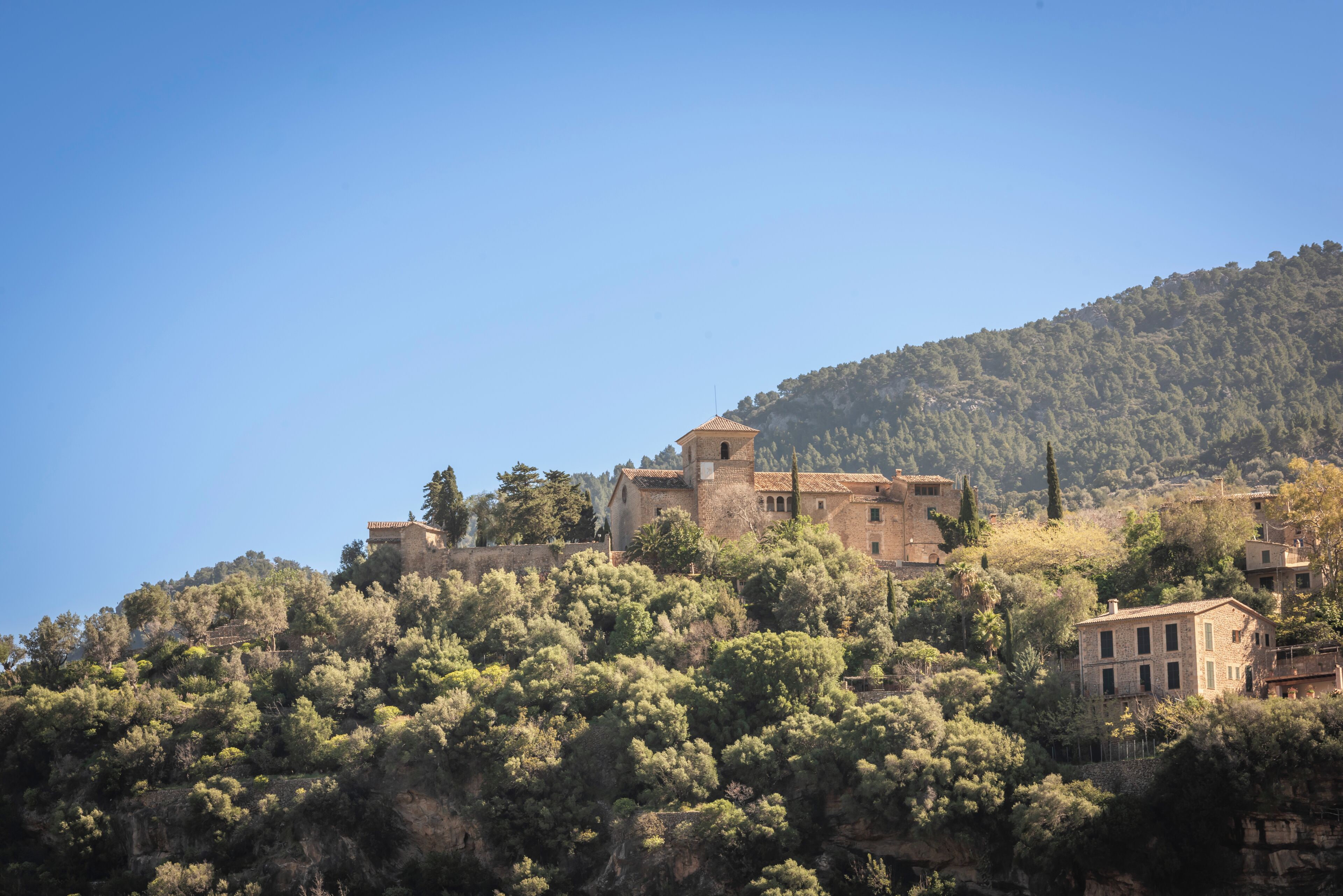 Un bâtiment situé sur une colline, composé de plusieurs structures, entouré d’une forêt dense et surplombant un ciel dégagé.