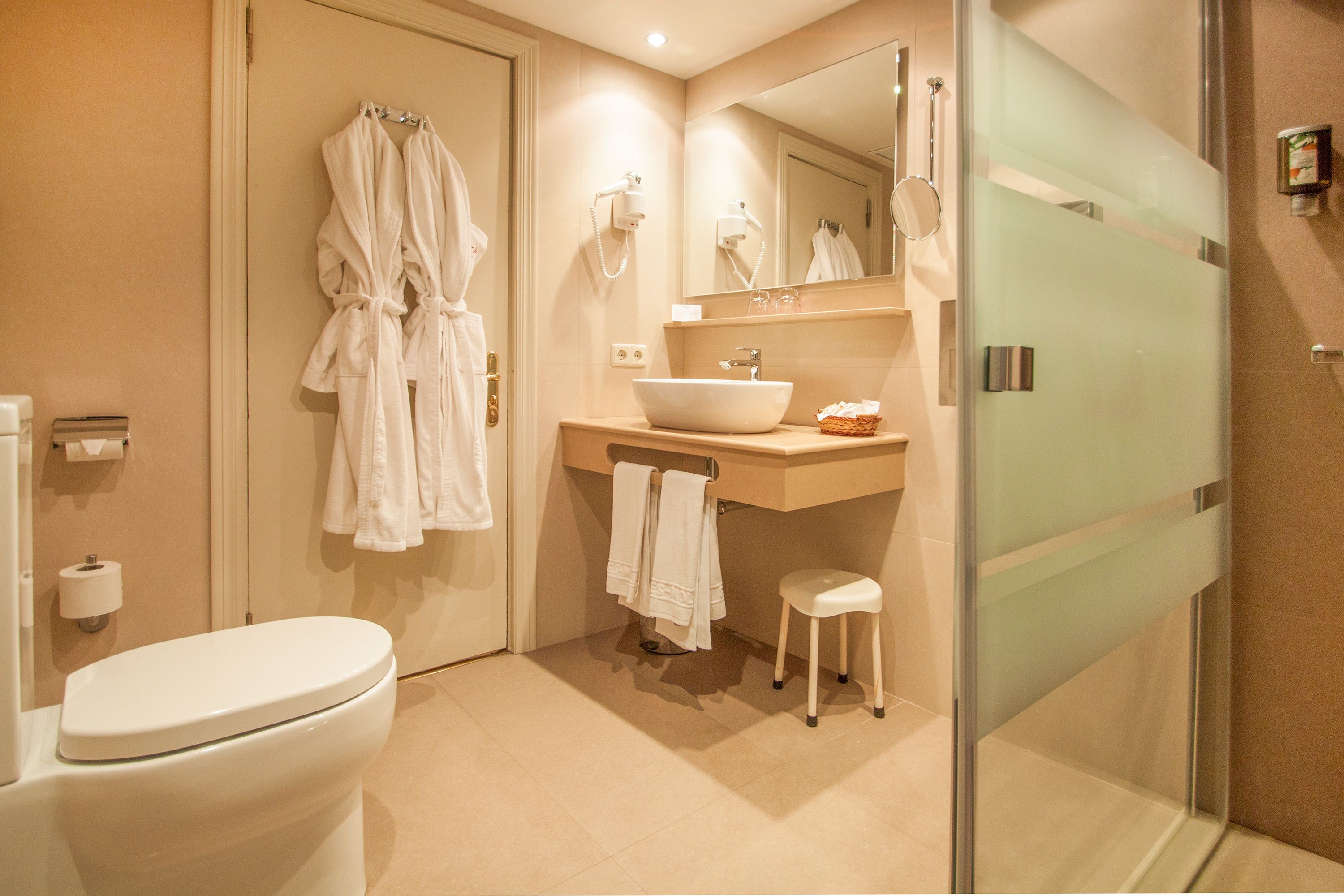 Une salle de bain moderne comprenant des toilettes, un lavabo avec un grand miroir et une douche à parois de verre.