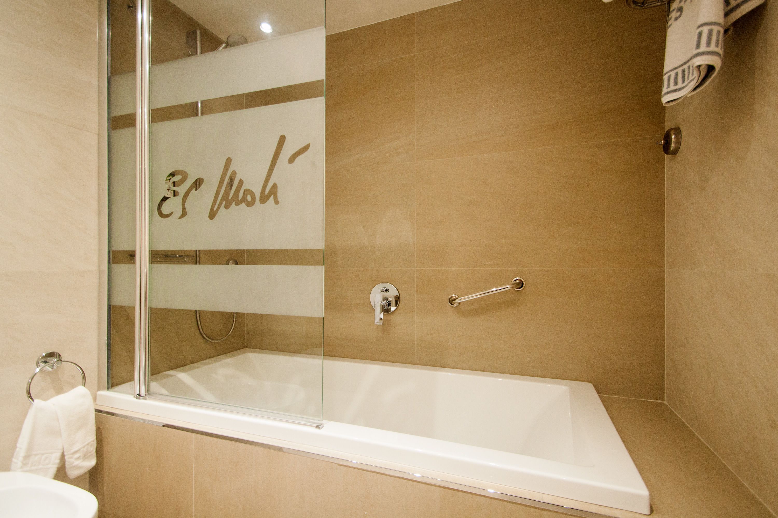 Une salle de bain moderne avec une douche à parois de verre, une baignoire blanche et des murs recouverts de carreaux de couleur beige.