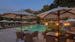A poolside area with lounge chairs and umbrellas, a pool, and stone flooring. - Es Moli Hotel (Deià)