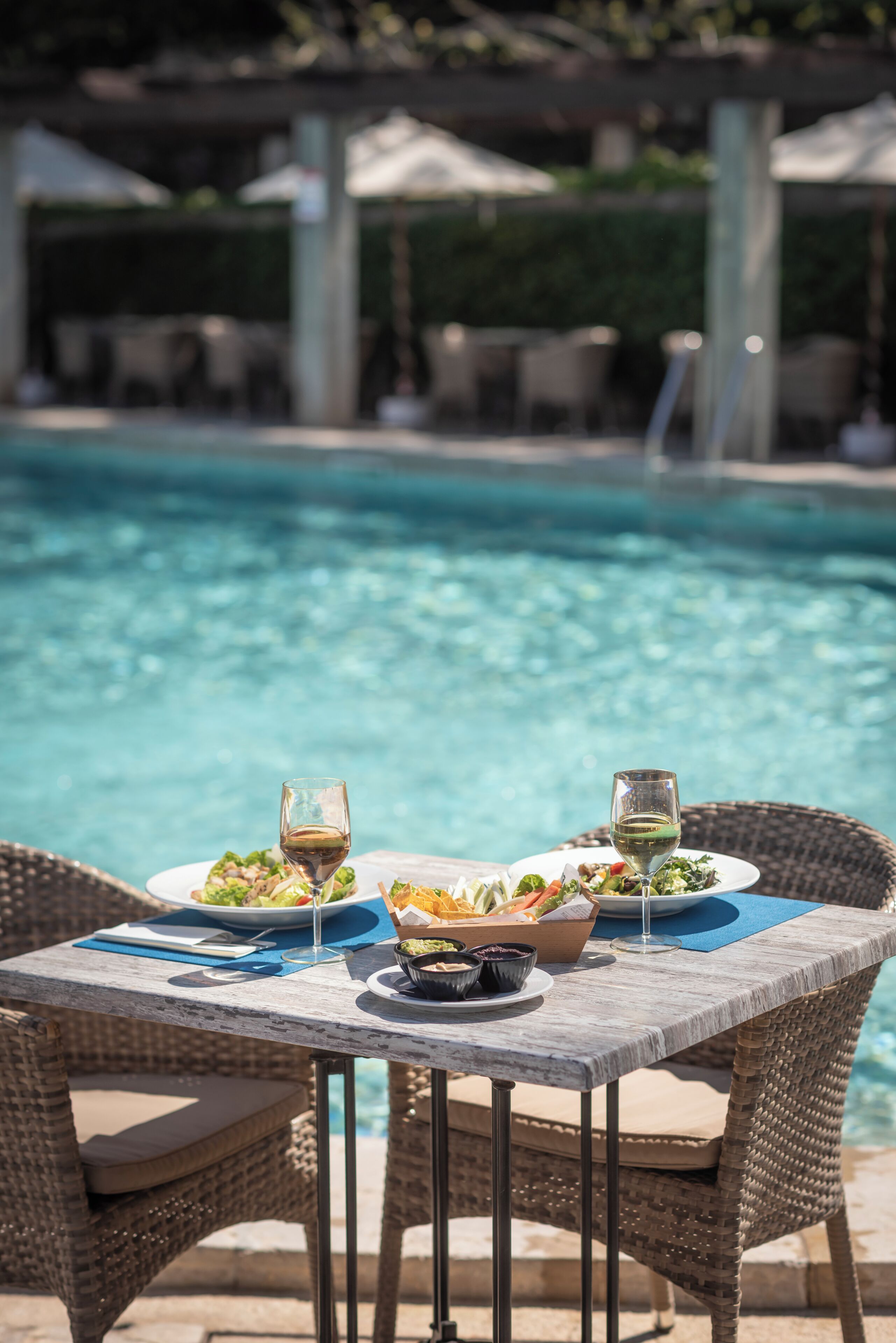 Un área de comedor al aire libre con una mesa preparada para dos, con vista a una piscina.