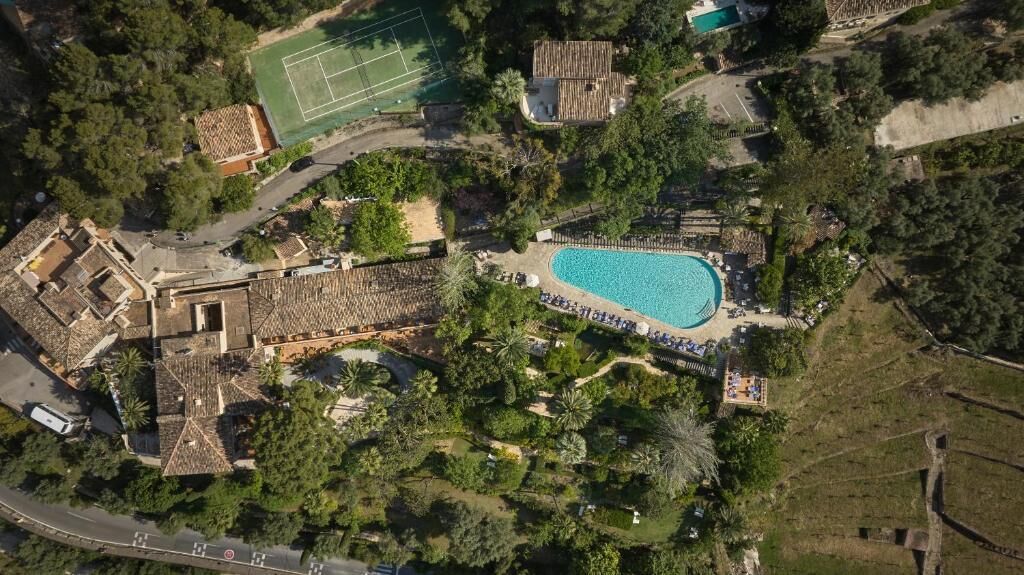 Ett flygbildsbild av ett semesterområde med en swimmingpool, tennisbanor och frodig grönska.
