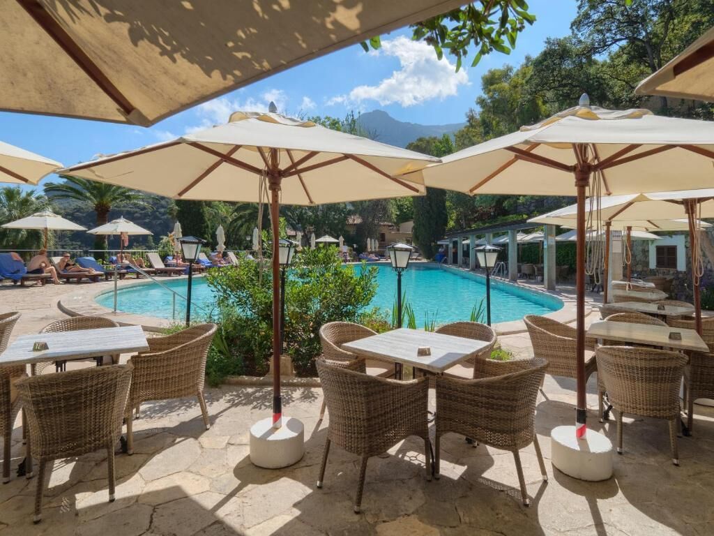 Un área junto a la piscina con sillones de descanso y sombrillas, una piscina y asientos al aire libre.