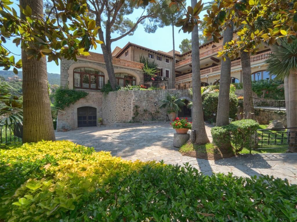 A courtyard with stone walls, potted plants, and a building with balconies.