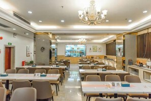 A spacious dining area with multiple tables and chairs, a chandelier, and a counter with a display of items. - Oriental Silk Hotel (Guangzhou)