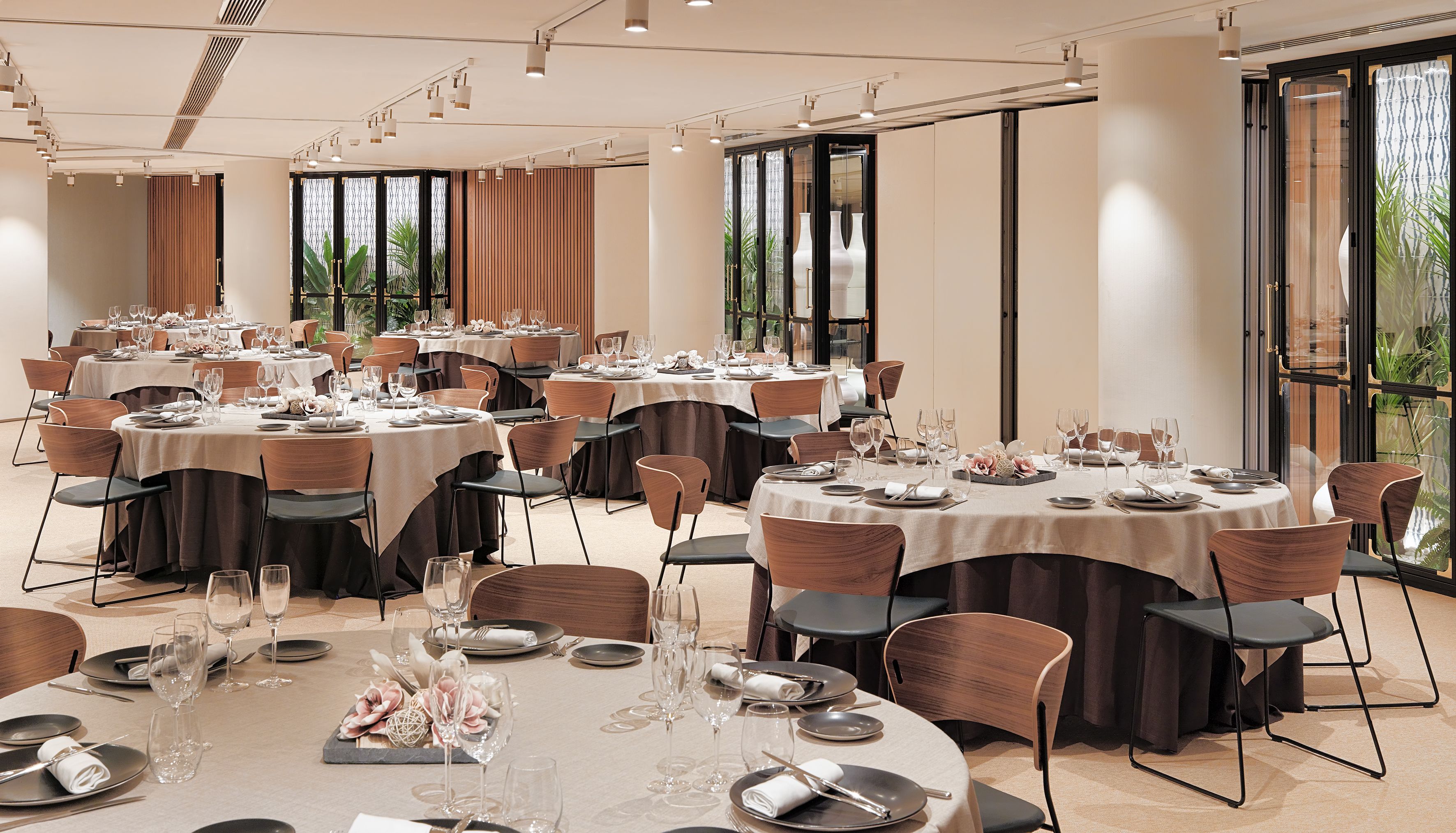Un amplio salón de banquetes con varias mesas redondas dispuestas para comer, con manteles blancos, sillas oscuras y una vajilla ordenada.