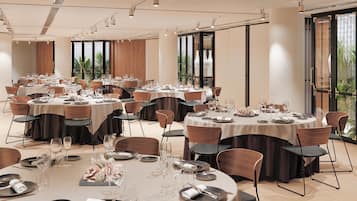 Un amplio salón de banquetes con varias mesas redondas dispuestas para comer, con manteles blancos, sillas oscuras y una vajilla ordenada.