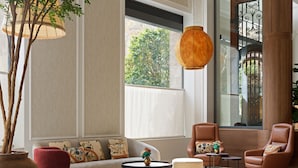 Un salon moderne comprenant un canapé, des fauteuils, des poufs, une table basse et une grande fenêtre donnant sur un paysage verdoyant.