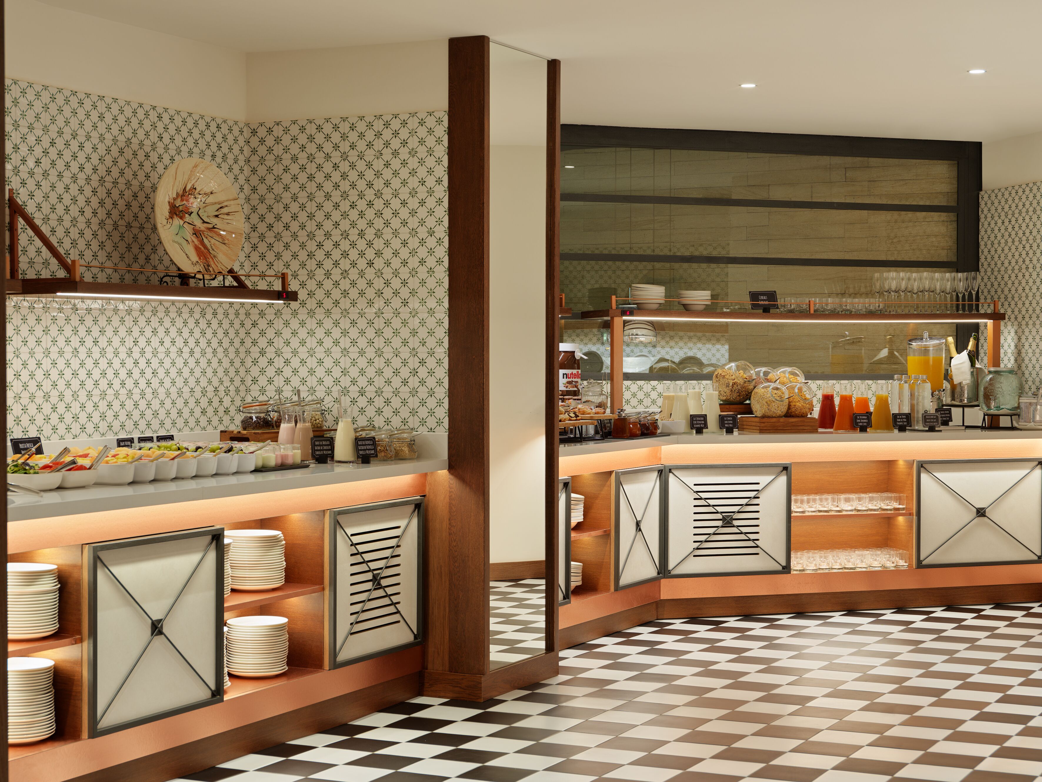 Um buffet de café da manhã com diversos alimentos e bebidas, parede com padrão e piso quadriculado.