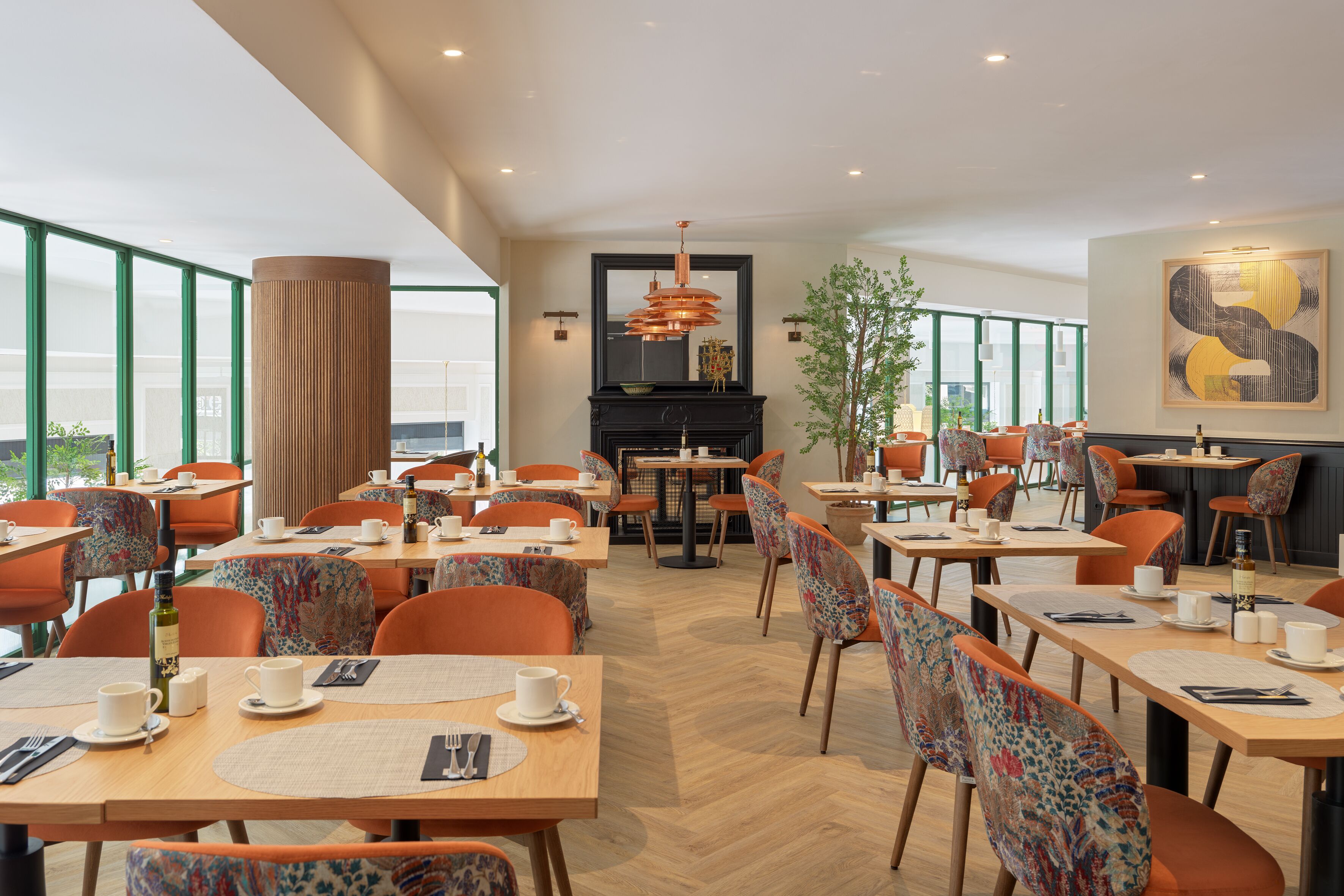 Un comedor moderno con mesas de madera, sillas anaranjadas, chimenea y amplios ventanales con vistas.