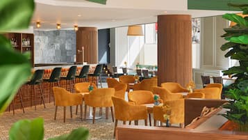 Un moderno vestíbulo de hotel con área de bar, zonas de estar y amplios ventanales que dejan entrar luz natural.