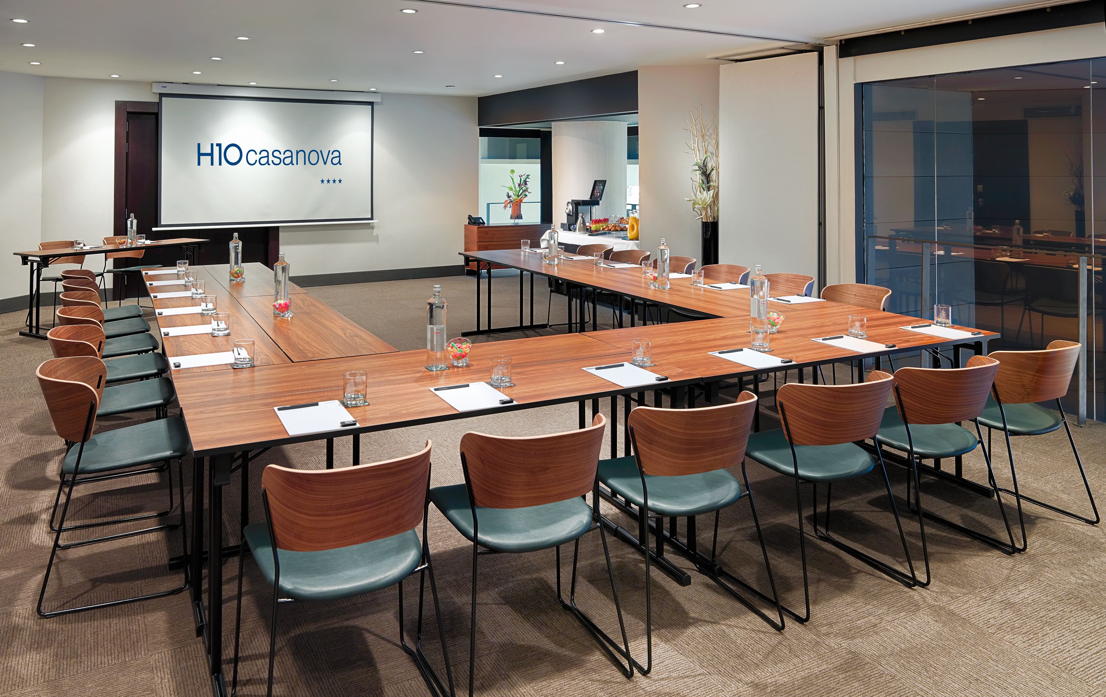 A conference room with a long table, chairs, and a projector screen displaying "HIO casanova".