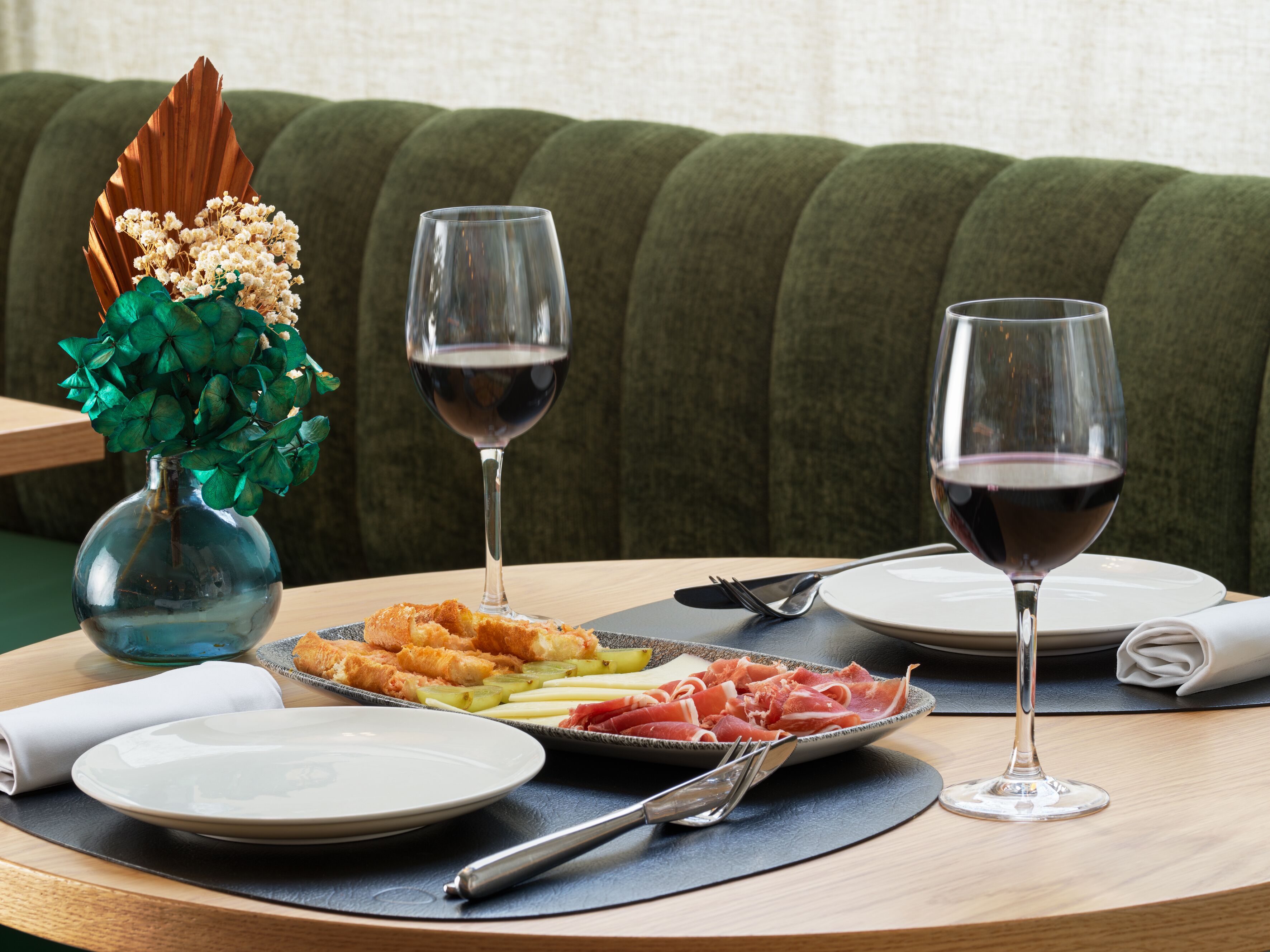 Una mesa con platos de comida, dos copas de vino y un florero con flores.