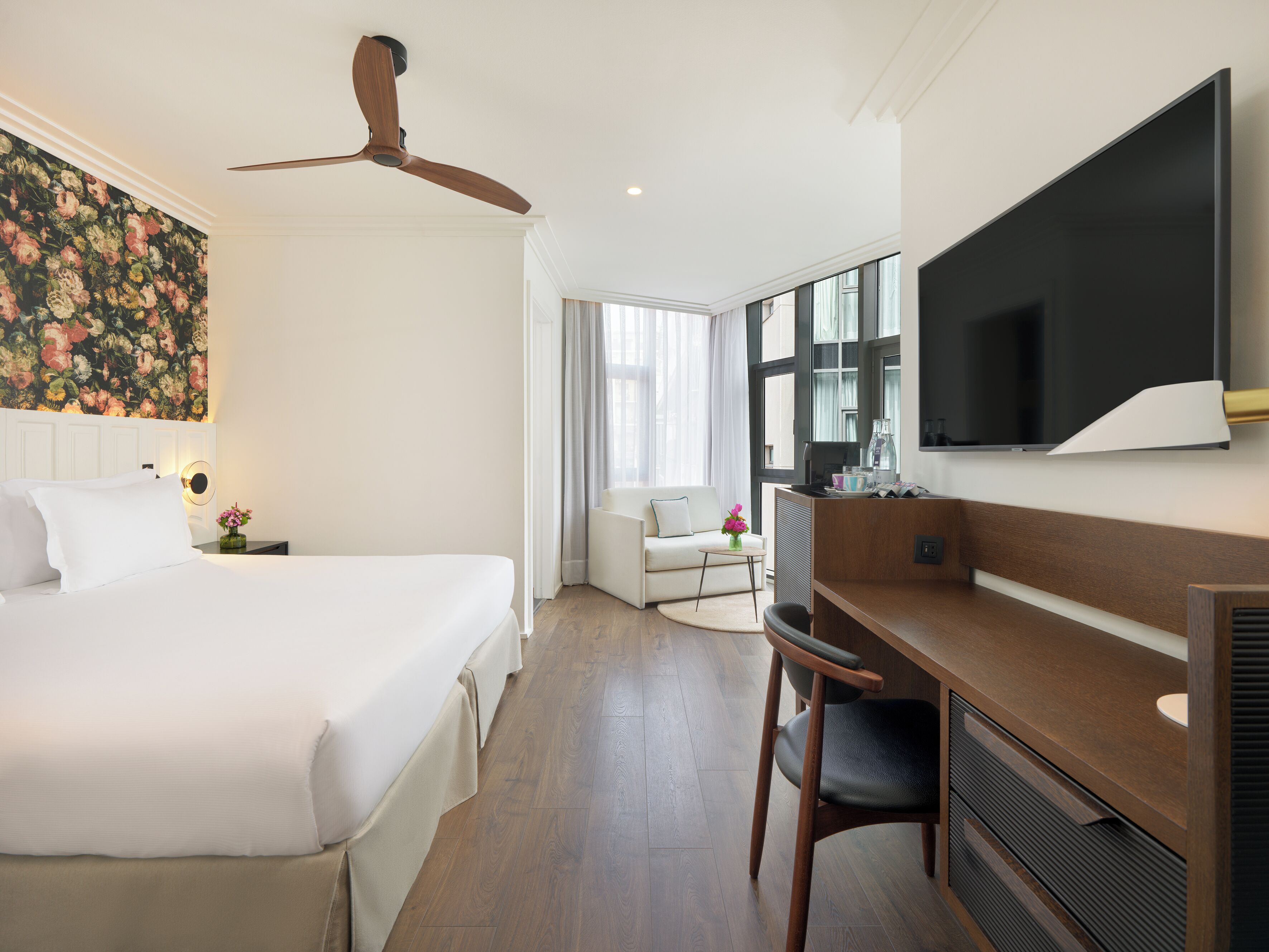 Una habitación de hotel con cama, escritorio, silla, televisor y ventilador de techo.