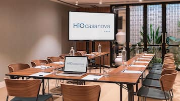 Un salón de conferencias con una larga mesa, sillas, una computadora portátil y una pantalla que muestra "HIO casanova".