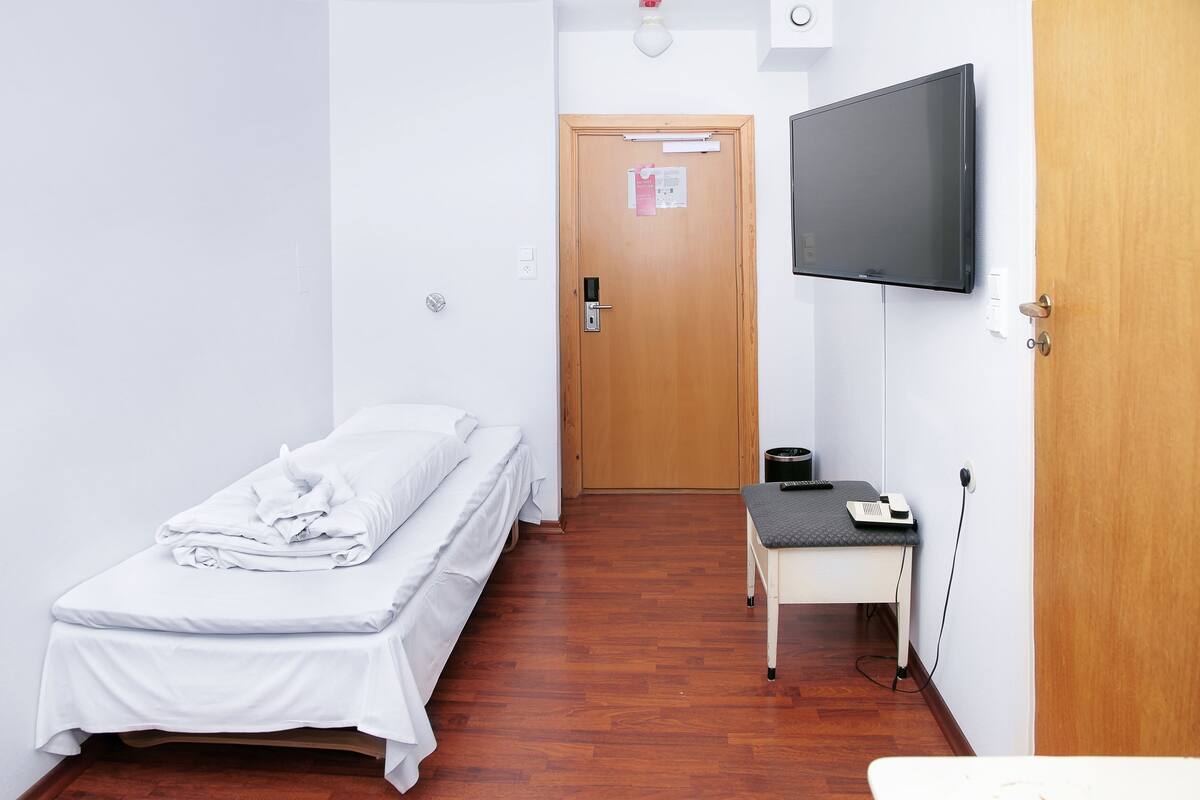 A small, clean room with a single bed, a desk, a chair, a television, and a door.