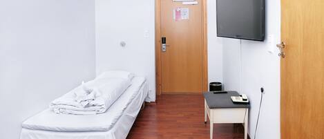 A small, clean room with a single bed, a desk, a chair, a television, and a door.