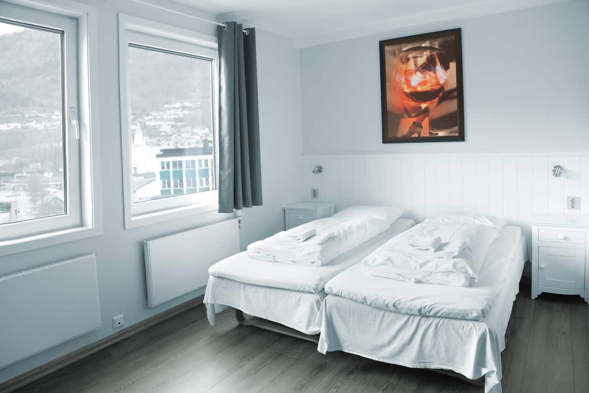 A bedroom with a bed, a nightstand, a window with curtains, and a wall-mounted picture.