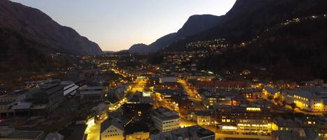 A town at dusk with illuminated buildings and a mountain backdrop.