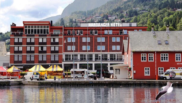 A red building with a sign reading "Hardanger Hotel" and a body of water in front.