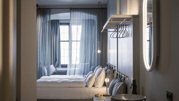 A modern hotel room with a large bed, a round mirror, a built-in vanity, and a window with sheer curtains.