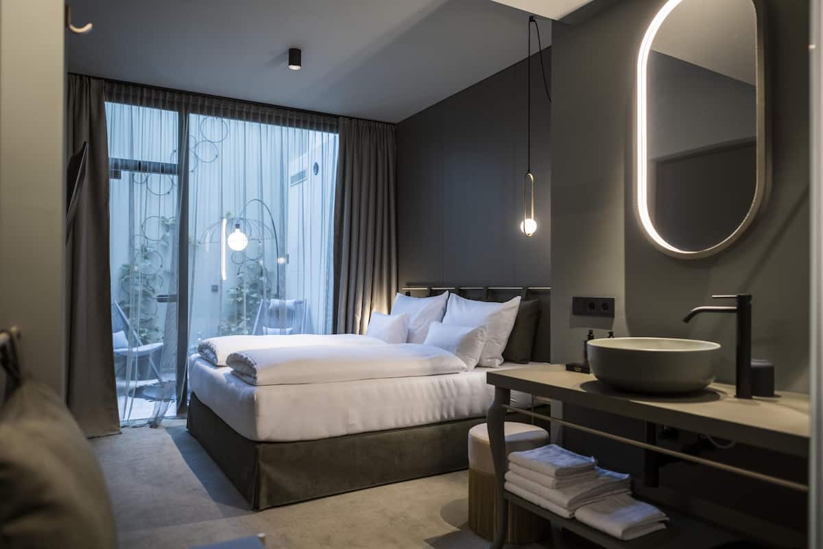 Habitació d'hotel moderna amb un llit gran, un mirall rodó, un lavabo rodó i vistes a l'exterior a través d'una finestra gran.
