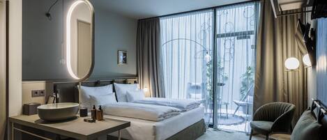 Une chambre d’hôtel moderne dotée d’un grand lit, d’un bureau avec un miroir, d’une chaise et offrant une vue sur l’extérieur grâce à de grandes fenêtres.